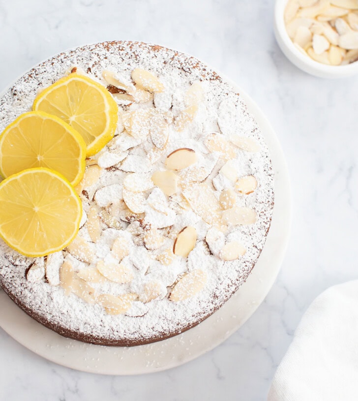 An almond cake dusted with powdered sugar and topped with lemon slices and sliced almonds