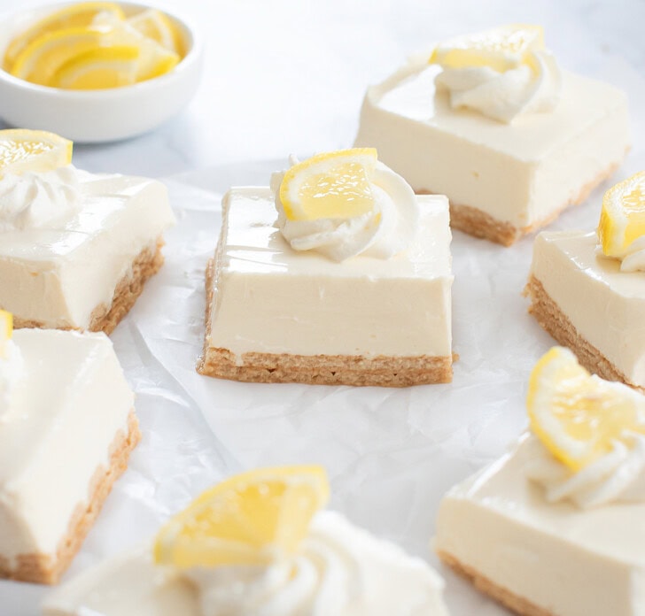 Lemon Yogurt Cheesecake Bars cut into squares with whipped cream and lemon pieces on top