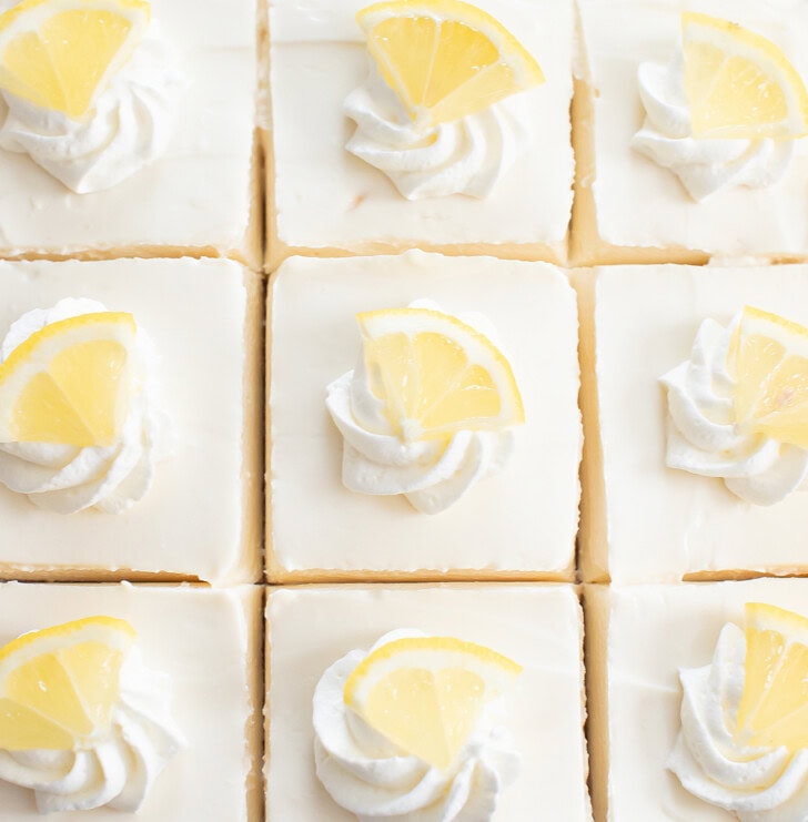 Lemon Yogurt Cheesecake Bars with whipped cream and lemon wedges on top