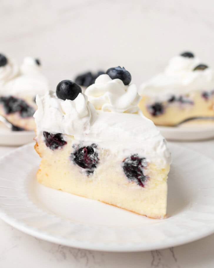 A slice of Blueberry Cottage Cheesecake with whipped cream frosting and fresh blueberries on top