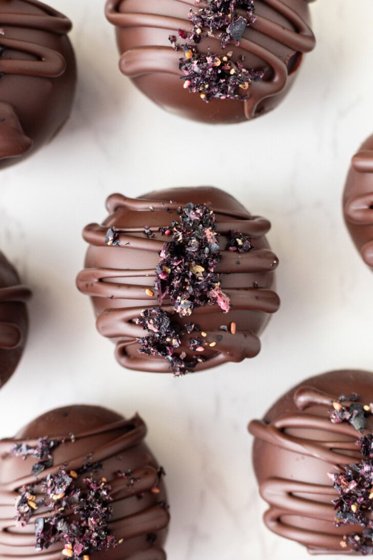 Blueberry balls coated in chocolate with a chocolate drizzle and freeze dried blueberries on top