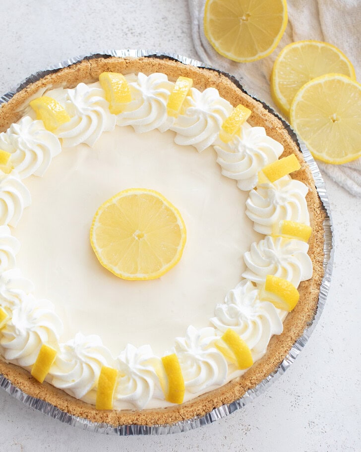 A lemon cheesecake with whipped cream around the edge and fresh lemon pieces