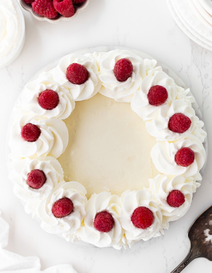 A cheesecake decorated with whipped cream and raspberries