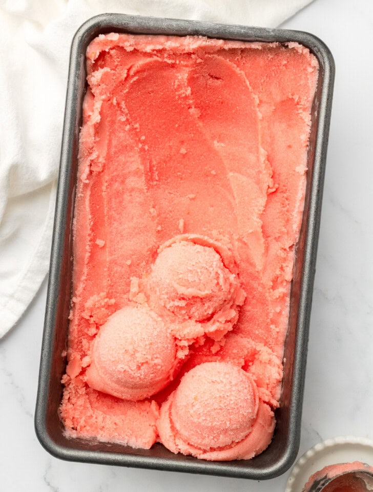 Watermelon ice cream in a loaf pan with three scoops on top