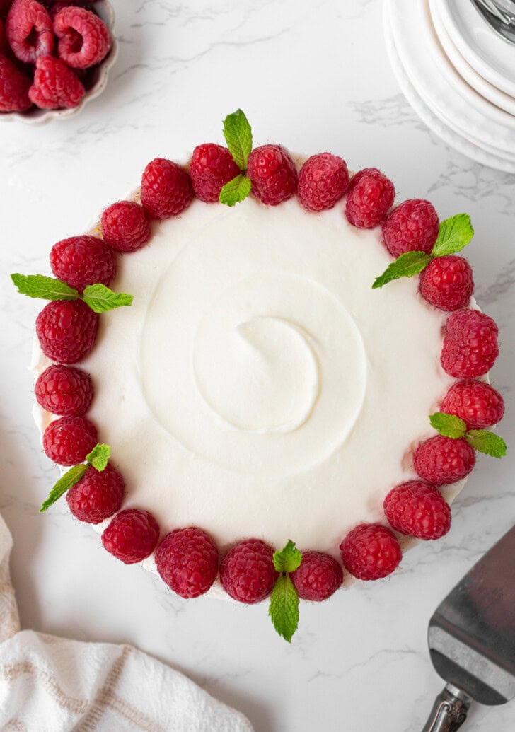 A cake decorated with cream cheese frosting and raspberries