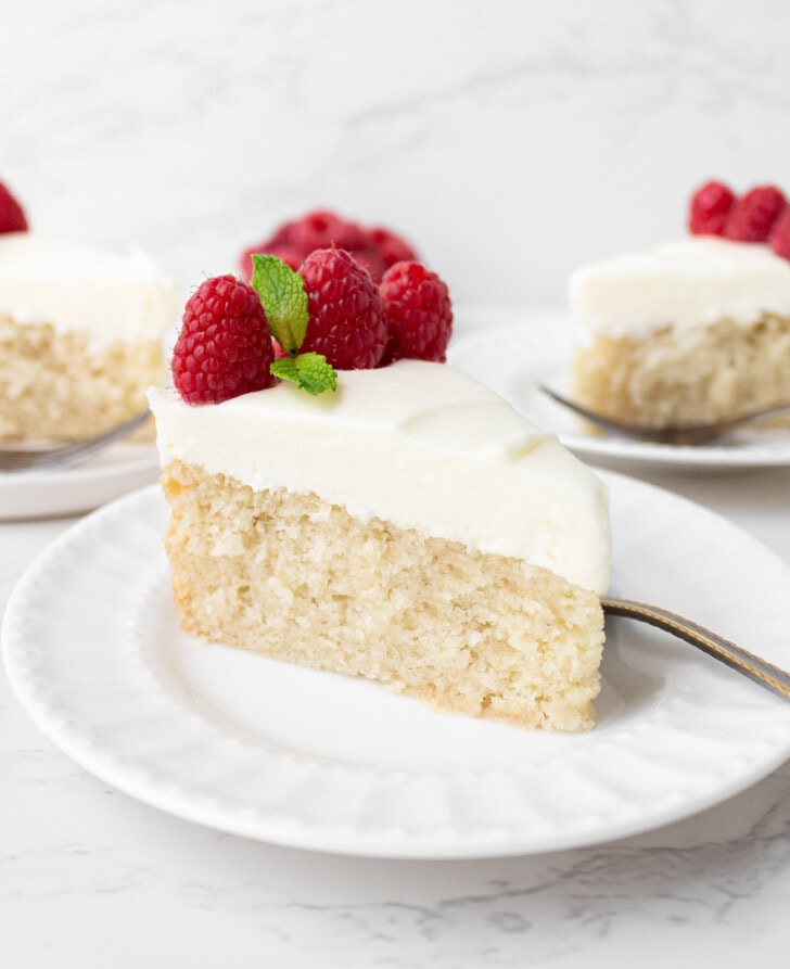 A slice of cake with frosting and fresh raspberries on top