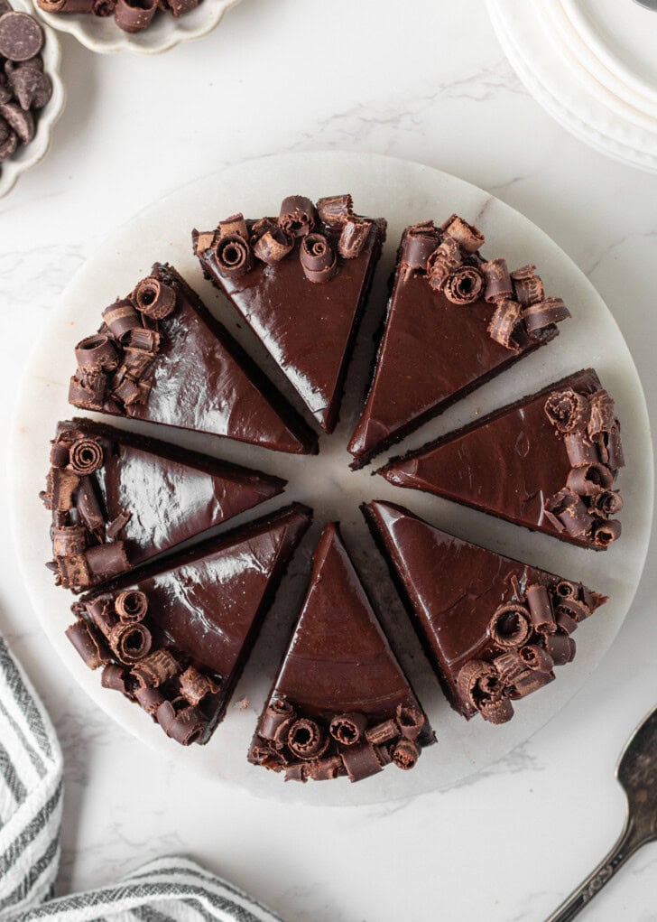 A chocolate cake cut into slices with chocolate ganache frosting and garnished with chocolate curls