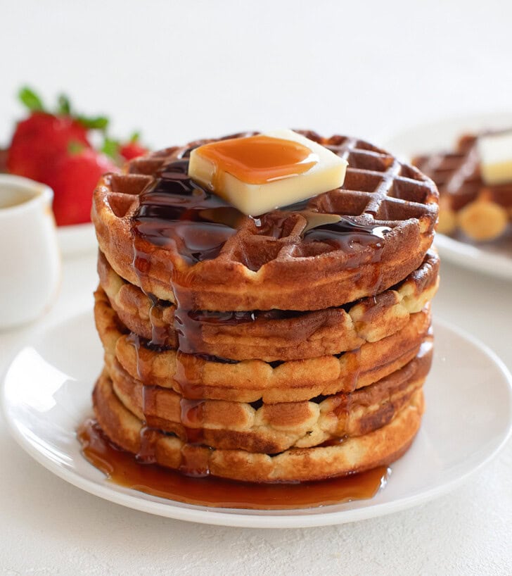 Stack of golden brown keto waffles topped with butter and maple syrup