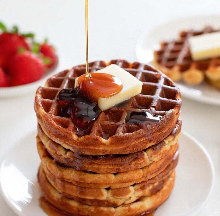 Maple syrup being poured on top of a stack of waffles