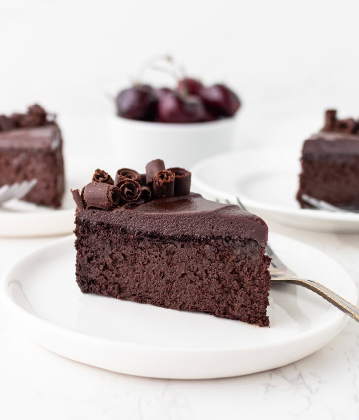 A slice of chocolate cake with chocolate ganache and chocolate curls on top