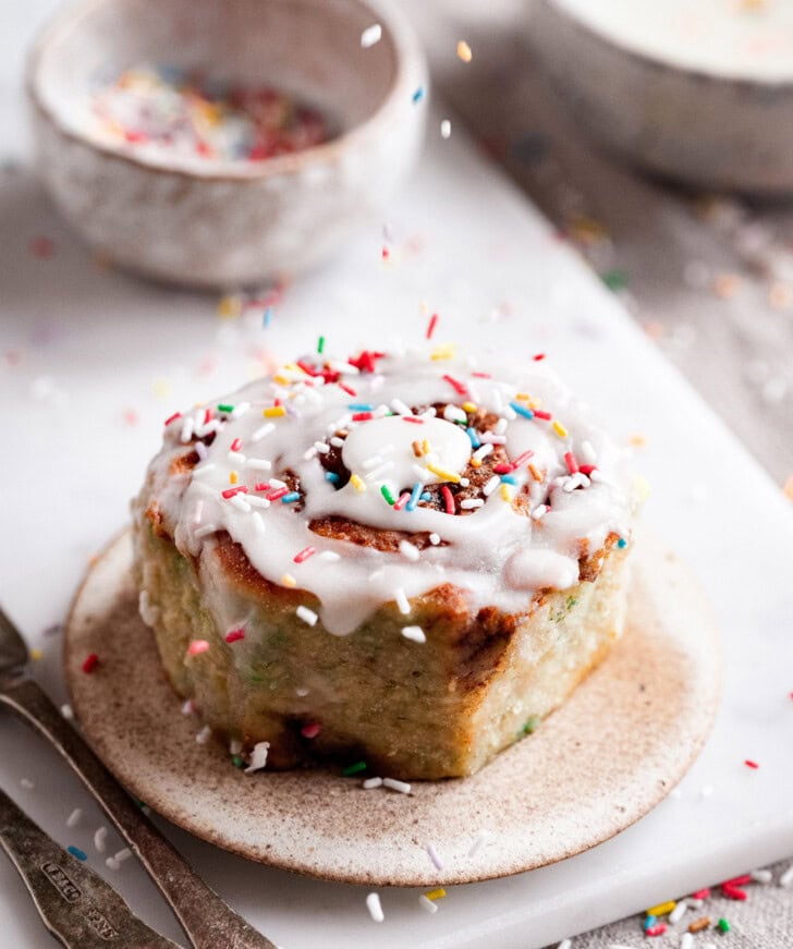 A cinnamon roll with rainbow sprinkles on a plate