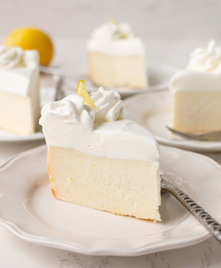 A slice of cheesecake with a whipped cream frosting and a slice of lemon on top