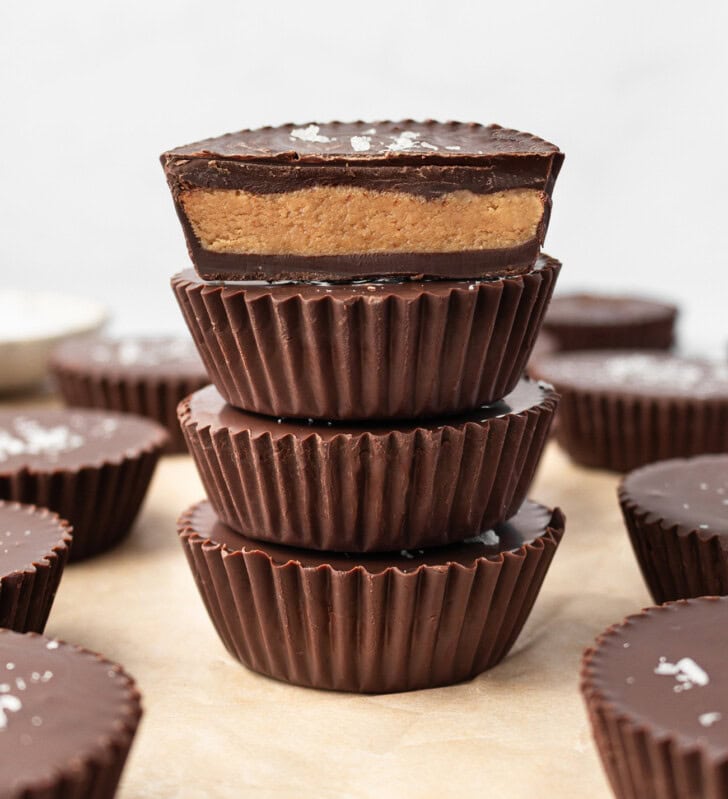 A stack of four chocolate peanut butter cups with the top one cut in half showing the center
